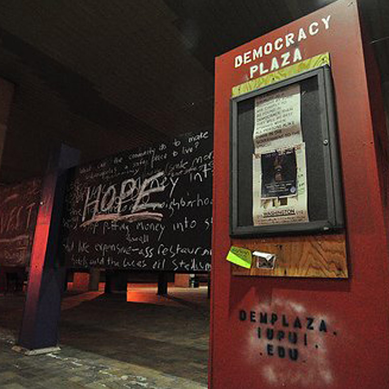 A red wall that says IUPUI Democracy Plaza attached to chalkboards.
