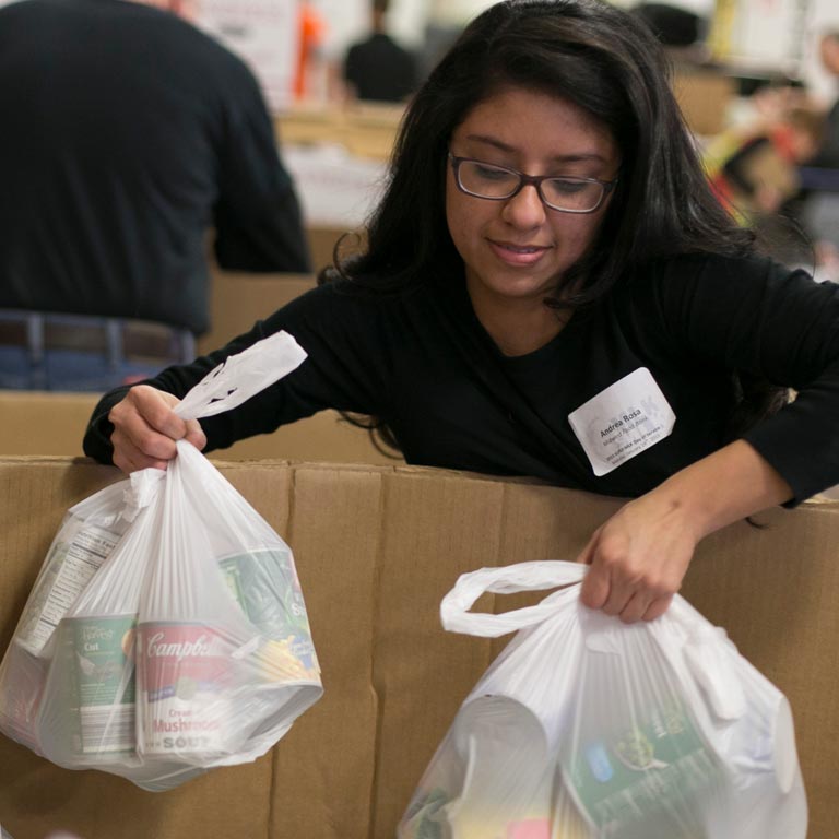 A person pulls  two grocery bags out of a brown box.