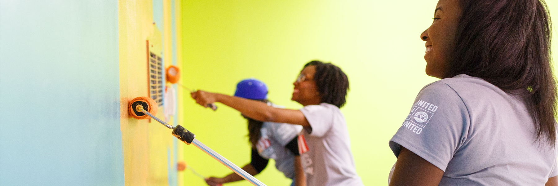 Three people paint a wall with rollers.