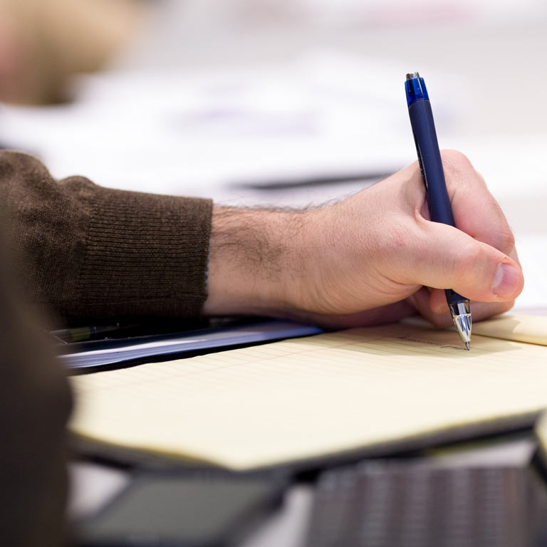 A hand writes on yellow paper with a blue pen.